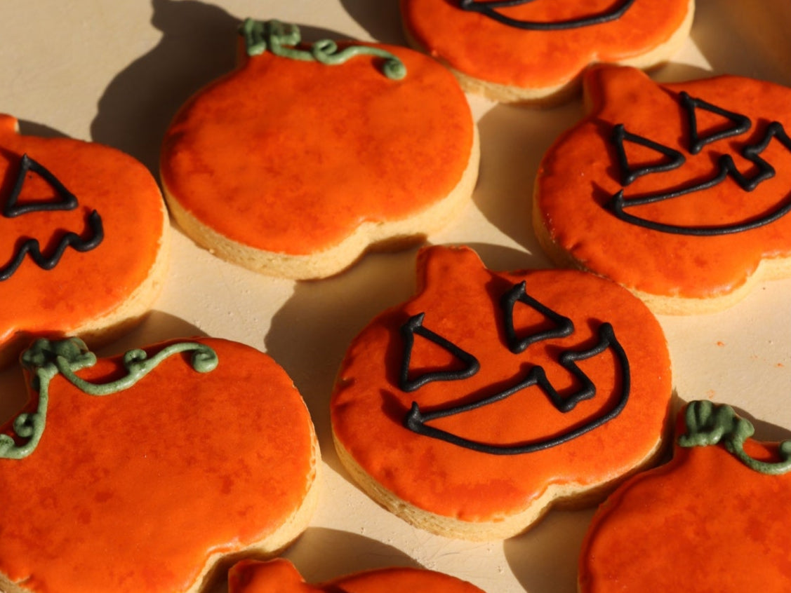 Halloween-themed cookies shaped like pumpkins with jack-o'-lantern faces on a tray.